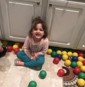 Nora sits on the ground amidst a pile up multi-colored toy balls.