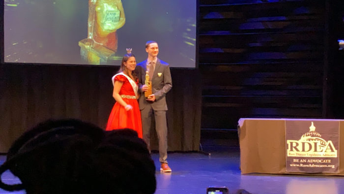 A young lady  in a red dress presents Aidan with his award.