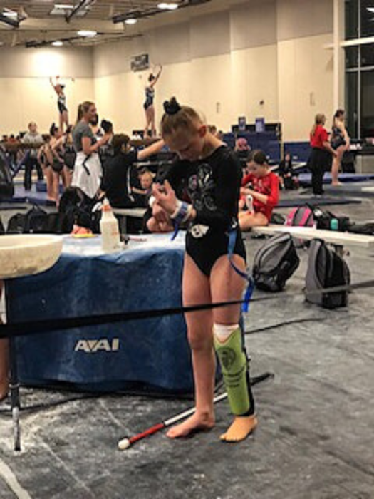 Jordan stands on her prosthetic foot and adjust her wrist bands at a gymnastic competition.