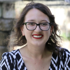 Head shot of Erica Green. She's wearing glasses, red lipstick and a black and white dress.
