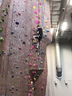 A teenage boys in black shirt and shorts is climbing a rock wall.