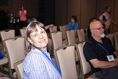 A woman with a blue lanyard around her neck sits on a chair in a row of chairs in a workshop at the NFED Family Conference. 