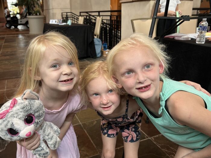 Three young girls affected by ectodermal dysplasia and have blonde hair have their arms around each other.