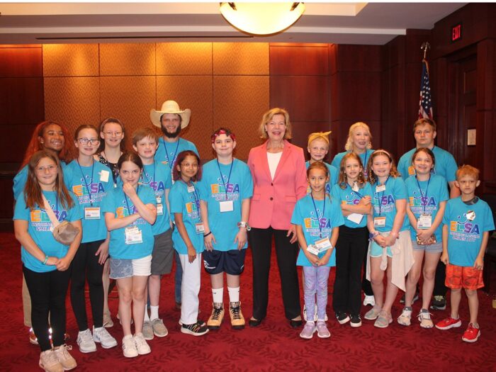 Senator Tammy Baldwin stand with numerous children and teens who are advocating for the Ensuring Lasting Smiles Act.