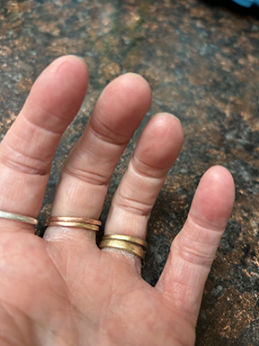 This photo shows the left hand of a woman with palm side up. She's wearing three gold rings. In this photo, she has lotion and the skin on the fingerprints is not as dry.