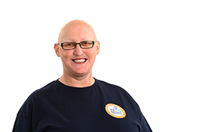 A woman who is bald and wearing black glasses wears a navy shirt with an NFED logo on the left chest. 