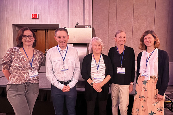 Four women and one man stand in front of a podium in a conference room. Each are wearing a name tag on a lanyard. The group announced the new XLHED clinical trial site.