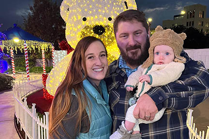 Beth and Peter are at a winter festival holding Matthew.