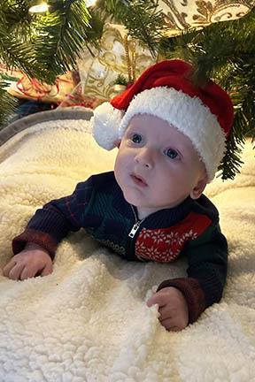 Matthew wears a Santa hat and lays under the Christmas tree.
