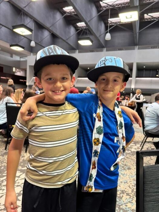 Two boys wearing baseball hats stand in a hotel restaurant with their arms around each other.