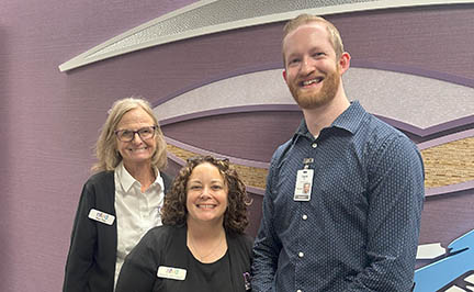 Three people are posed for a photo in front of a wall with a design on it in the hospital.