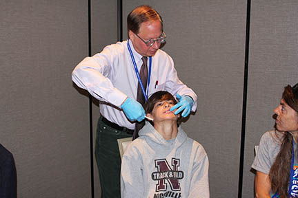 Dr. Stanford examines a young man's mouth and is looking at the mother seated beside him.