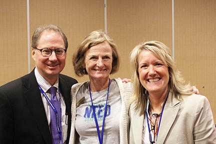 Three people are standing next to each other with their arms around one another. All are wearing a conference lanyard.