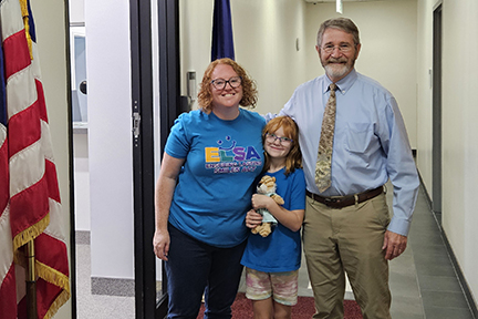 Tiffiny and her daughter stand with a legislative aide in the hall outside of the legislative office. The U.S. flag stands in the foreground.