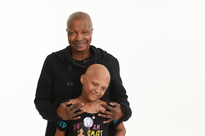 A mom stands behind her school age daughter and has her hands on her shoulders.