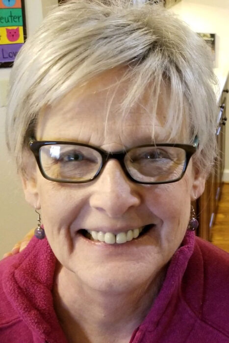 A woman is wearing a fuchsia shirt, black glasses and a wig that has short blonde hair.