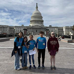 Five youth stand outside the U.S. Capitol Building. Three girls and two boys.
