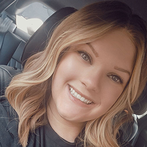 A young woman's headshot. She has a wig on that is wavy blonde hair.