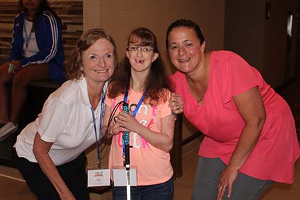 Mary and her daughter have arms around a young woman who is holding her cane.