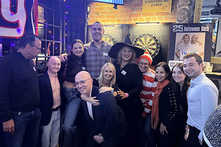 This group of people are dressed up or waring costumes at the Halloween Bash which is in the back groom of a bar.