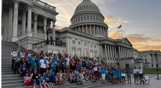 Advocates for the Ensuring Lasting Smiles Act stand and sit on the steps of the U.S. Capitol Building in Washington DC with the sun setting behind the building.