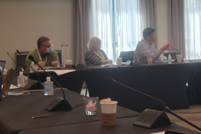 Three people, including Dr. Butcher, sit at a Conference table at a meeting.