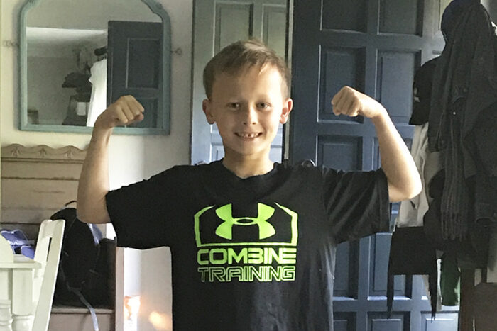 Finnegan, as a youth, is flexing his muscles, wearing a black Under Armour shirt that says Combine Training.