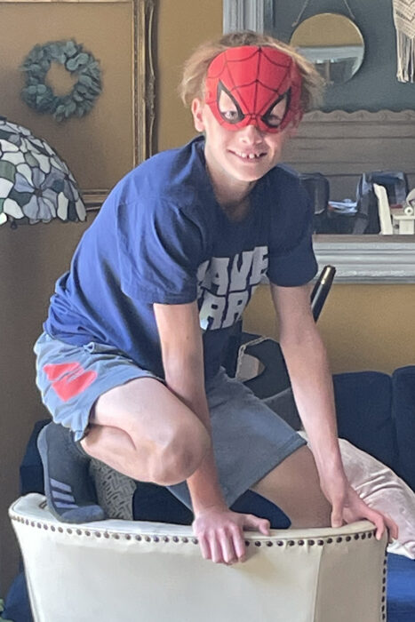 Finnegan is wearing his Spiderman mask, a blue t-shirt and gray shorts. He's standing on a chair.