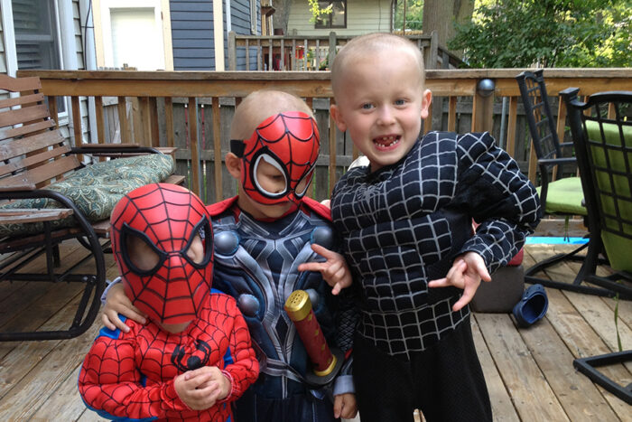 Finnegan and his two brothers are all wearing Spiderman costumes.. They are standing on their back deck.