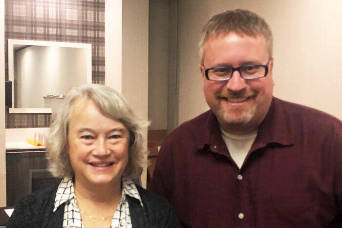 A woman stands next to Dr. Butcher in a conference room.