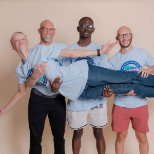 Three men are holding a teenage boy across their arms.