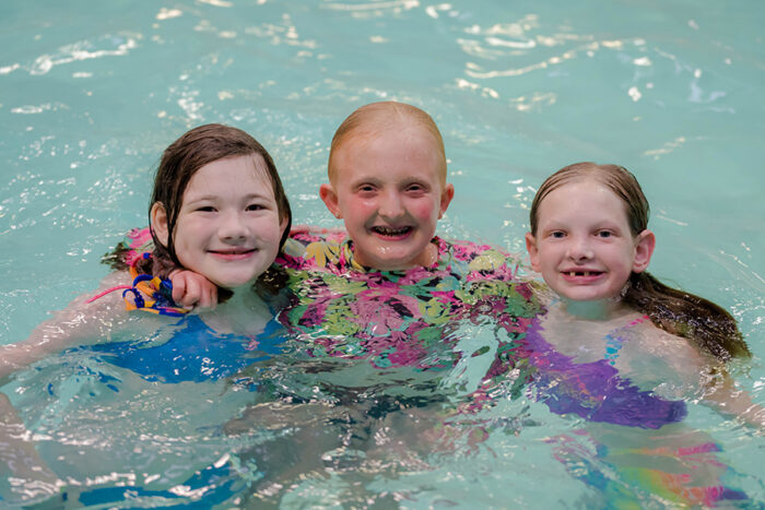 Three girls are in the swimming pool with their arms around each other.