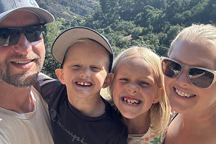 The parents hold the two kids with trees in the background.