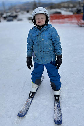 A boy is wearing a helmet and snow skis outside in the snow.