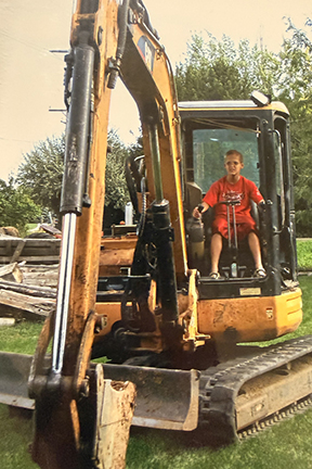 Sam as a boy is sitting on a construction digger.