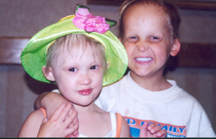 Sam as a young boy has his arm around a young girl who also has HED. She's wearing a green hat with a pink flower. They are at the NFED family conference. 