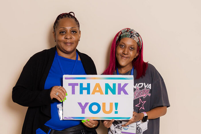 A mom and daughter are standing side by side holding a sign that says, Thank You.