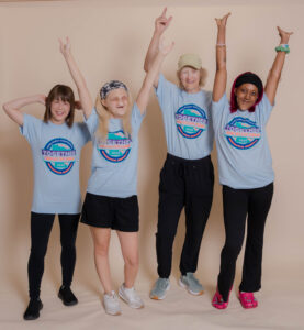 Four women affected by EEC syndrome stand side by side with their arms above their head. They are all wearing the same tshirt.