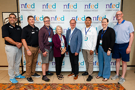 A group of people stand in front of an NFED backdrop.
