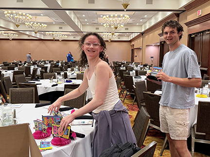 A teenage girl is putting out 1980s decorations on a table in a dining room. Her brother is behind her holding one of the decorations.