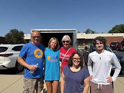 Five NFED Family Conference volunteers are standing in front of a trailer of boxes that is headed to the event.