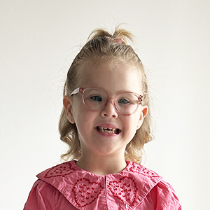 A head shot of a young girl who is wearing glasses and a pink shirt with a collar. She's affected by a TSPEAR-related type of ectodermal dysplasia.