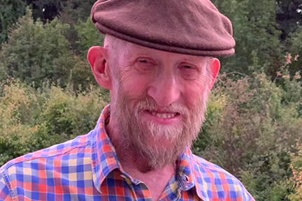 A head shot of Jack who is wearing a cap and a plaid button up shirt.