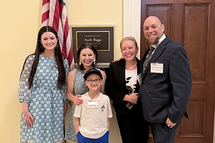 Advocates stand with a staffer in front of a Congressional office with the U.S. flag hanging behind them.