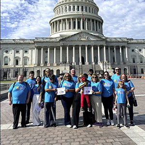 A group of ELSA advocates in teal ELSA shirts pose in front of the U.S. Capitol building.