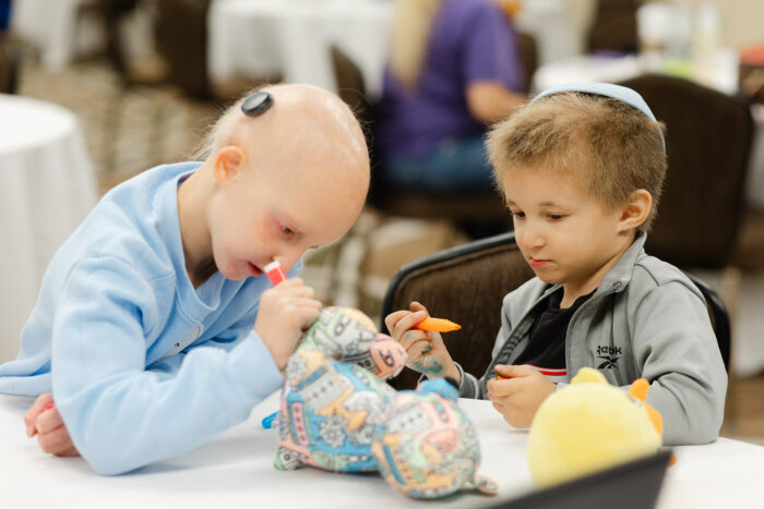 Two children are using markers to color a stuffed teddy bear.