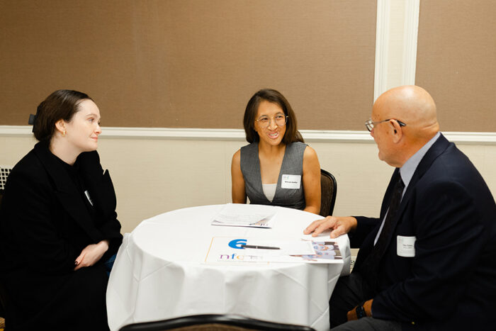 Three people are seated at a round conference table talking.