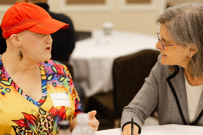 A woman in a red ball cap shares a story with a doctor at a round conference table.