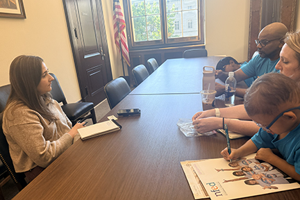 A woman sits across a conference table from a family in a congressional office. The young boy is coloring.